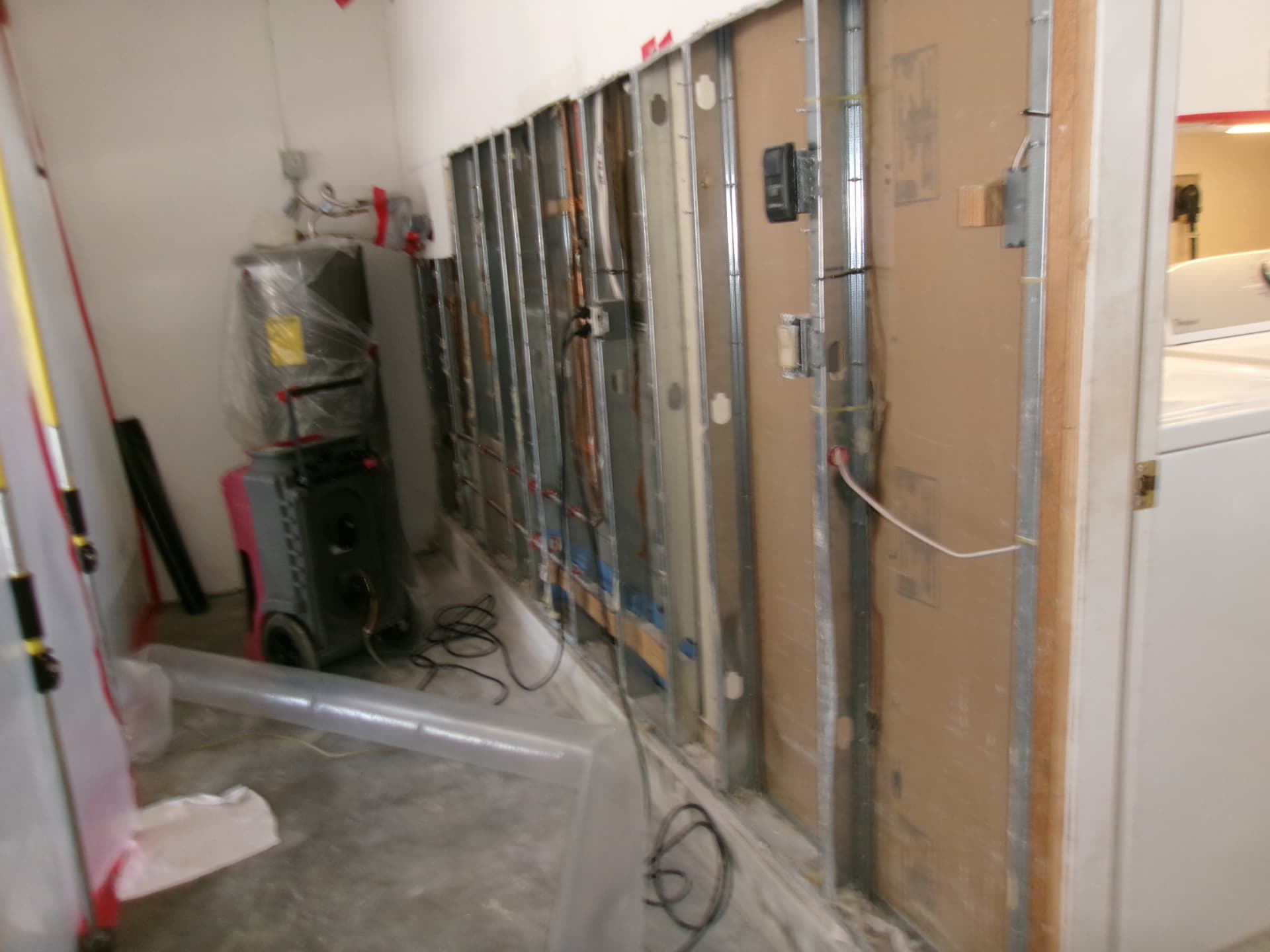 Commercial dehumidifier and air mover drying exposed studs in a stripped hallway